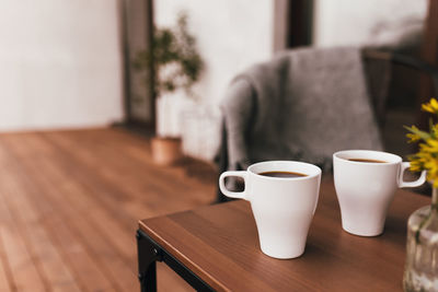 Two cups of coffee on table on wooden brown terrace during evening sunset with blurred background