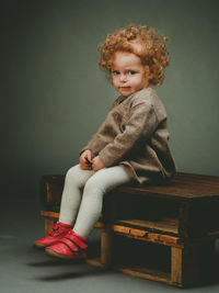 Cute baby girl sitting on chair against wall