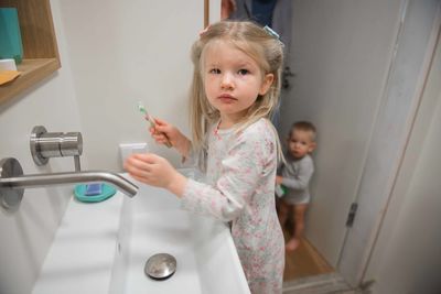 Portrait of girl holding toothbrush by baby boy in bathroom at home