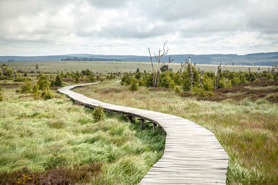 Boardwalk leading towards landscape against sky