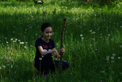 Portrait of girl kneeling with stick amidst dandelions on field