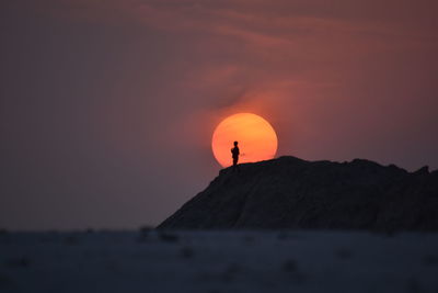 Silhouette rock in sea against sky during sunset