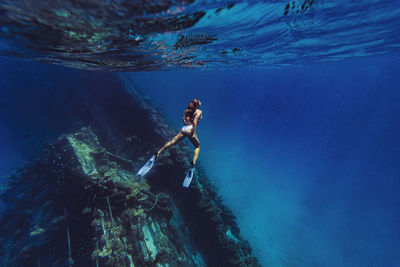 Woman swimming underwater by shipwreck in sea