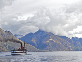 Boat sailing on sea by mountains against sky