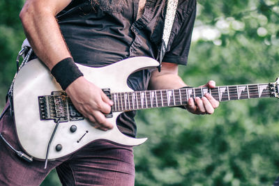 Midsection of man playing guitar while standing outdoors