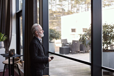 Senior businessman listening music while standing by window in office