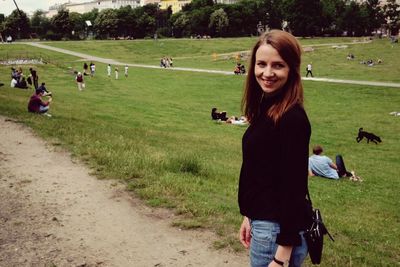 Young smiling woman standing on pathway by grassy field at park