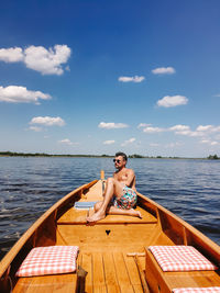 Full length of shirtless man sitting on boat over sea