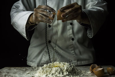 Midsection of chef preparing food against black background