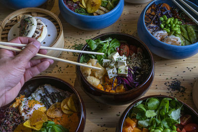 Man picking food by hand with chopsticks into the poke bowl on a wooden table.