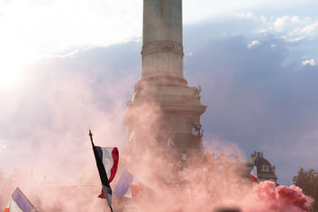 Low angle view of smoke by column against cloudy sky