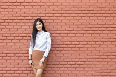 Portrait of young woman standing by brick wall