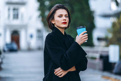 Portrait of woman holding smart phone while standing in city