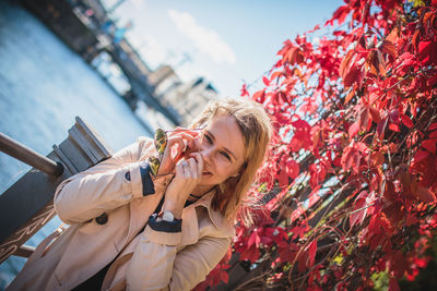 Young woman using phone while leaning on railing by creeper plant