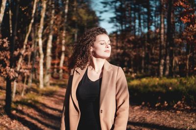 Beautiful young woman looking away while standing on tree in forest