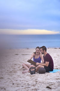 Man and woman sitting on sand against sea at beach