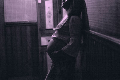 Side view of woman standing by window at home