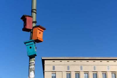 Low angle view of birdhouse against building against clear blue sky