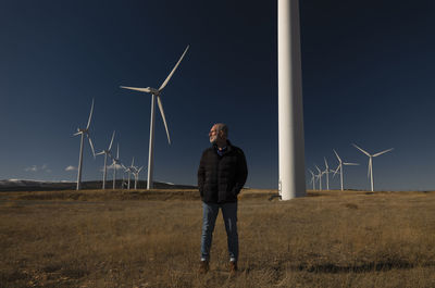 Adult man in winter cloth with modern windmills against blue sky. shot in castilla la mancha, spain