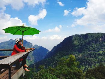 Woman sitting at observation tower with mountains in background against sky