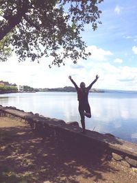 Rear view of woman with arms raised standing at lake against sky