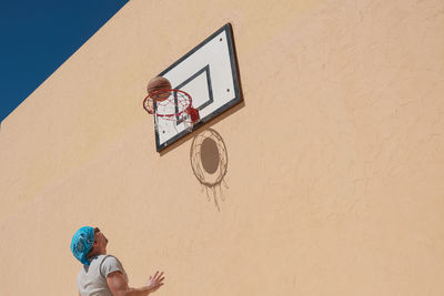 Low angle view of basketball player and basketball hoop against yellow wall 