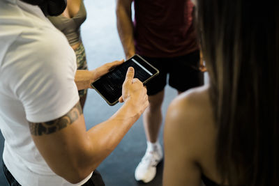 Man with digital tablet talking with male and female friends at gym