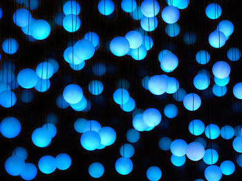 Illuminated blue light bulbs hanging against black background