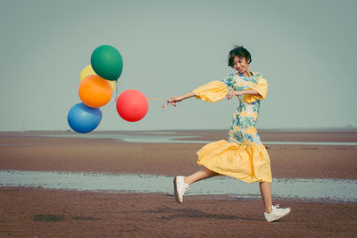 Side view of young woman with colorful helium balloons running at beach