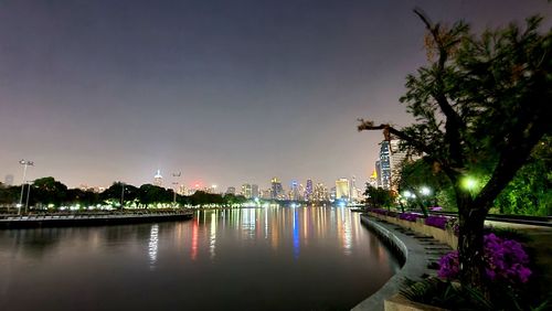 Illuminated city by river against sky at dusk