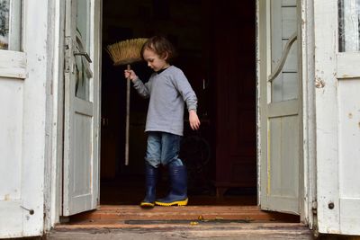 Full length of boy holding broom on doorway