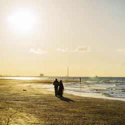 Silhouette couple walking on shore at beach