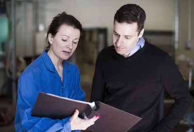 Mid adult female technician explaining documents to client in industry