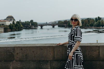 A young blonde girl stands on a bridge on a summer day.
