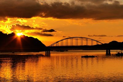 Silhouette bridge over river against sky during sunset