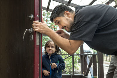 Man repairing door with son in background