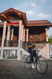 Man riding bicycle on house by building against sky