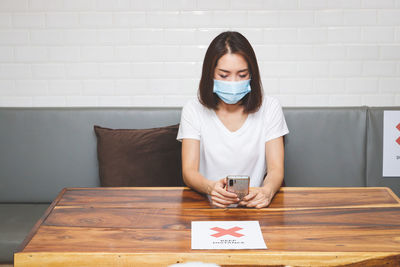 Portrait of young woman using phone while sitting on table