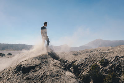 Man standing on rock against clear blue sky