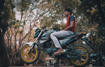 Young man sitting on bicycle against trees