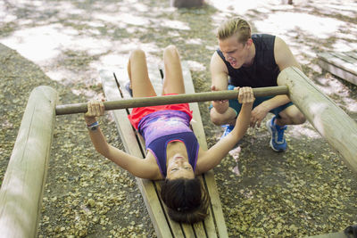 Man encouraging woman in lifting wooden weight at outdoor gym