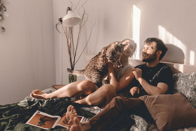 Happy couple playing with cat on bed at home