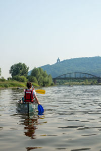 Teenage bow rowing in river against clear sky