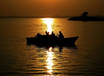 Silhouette men in lake against sky during sunset