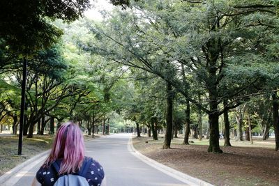 Rear view of woman walking on road along trees