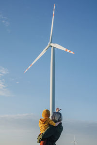 Mother showing wind turbine to son in front of sky