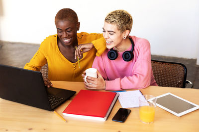 Cheerful lesbian couple working over laptop on table at home