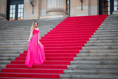 Female model wearing pink evening gown while standing on steps