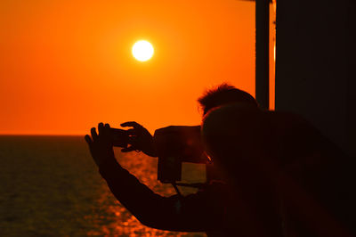 Rear view of silhouette man photographing at sunset