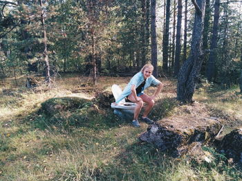 Woman in chair position over abandoned toilet seat in forest